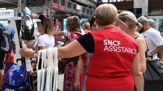 Une agente SNCF assiste des passagers en gare.